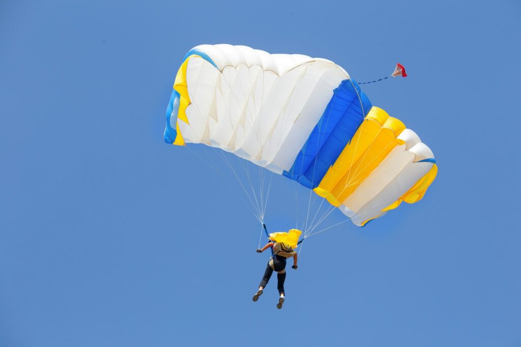 Skydiver under canopy of yellow with blue parachute in cloudless sky